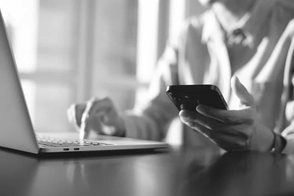 Person sitzt mit Smartphone in der Hand an einem Laptop
